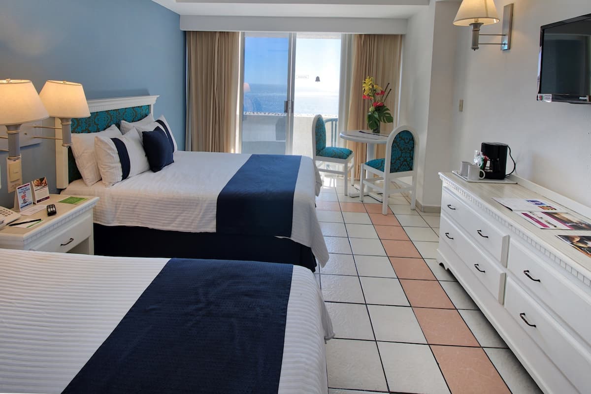Una habitación de hotel con dos camas, un escritorio, una silla, televisión y vista al océano.