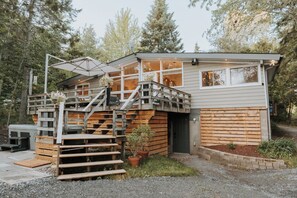 A modern cabin with a wooden exterior, a covered outdoor seating area, and a staircase leading to a deck. - 6BR Lakefront Muskoka Sunset Retreat w/ Hot Tub, Dock & Firepit (Utterson)