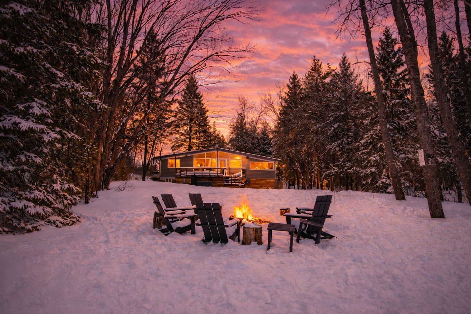 Winter sunset from 3 Mile Lake, with the cottage lit warmly and a cozy bonfire.