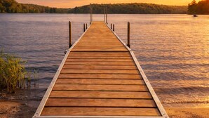 Eine Holzsteg, der sich in ruhiges Wasser erstreckt, mit einem Sonnenuntergang im Hintergrund.
