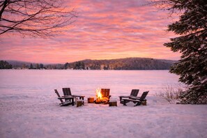 A snowy landscape with a fire pit and two chairs facing a sunset over a frozen lake. - 6BR Lakefront Muskoka Sunset Retreat w/ Hot Tub, Dock & Firepit (Utterson)