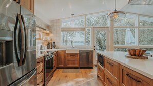 Eine moderne Küche mit Holzausstattung, Edelstahlgeräten und großen Fenstern mit Blick auf Bäume.