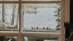 Blick aus einem Fenster auf einen See mit Stühlen und einem Tisch auf der Terrasse.