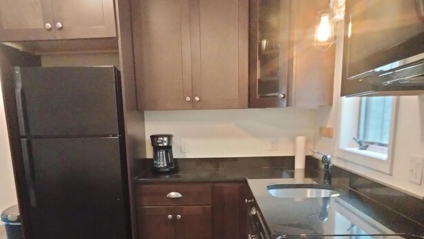 Een keuken met houten kastjes, een zwarte koelkast, een koffiezetapparaat en een raam met uitzicht.