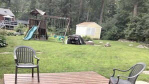 Een houten terras met twee stoelen, een schommel en een glijbaan op de achtergrond.
