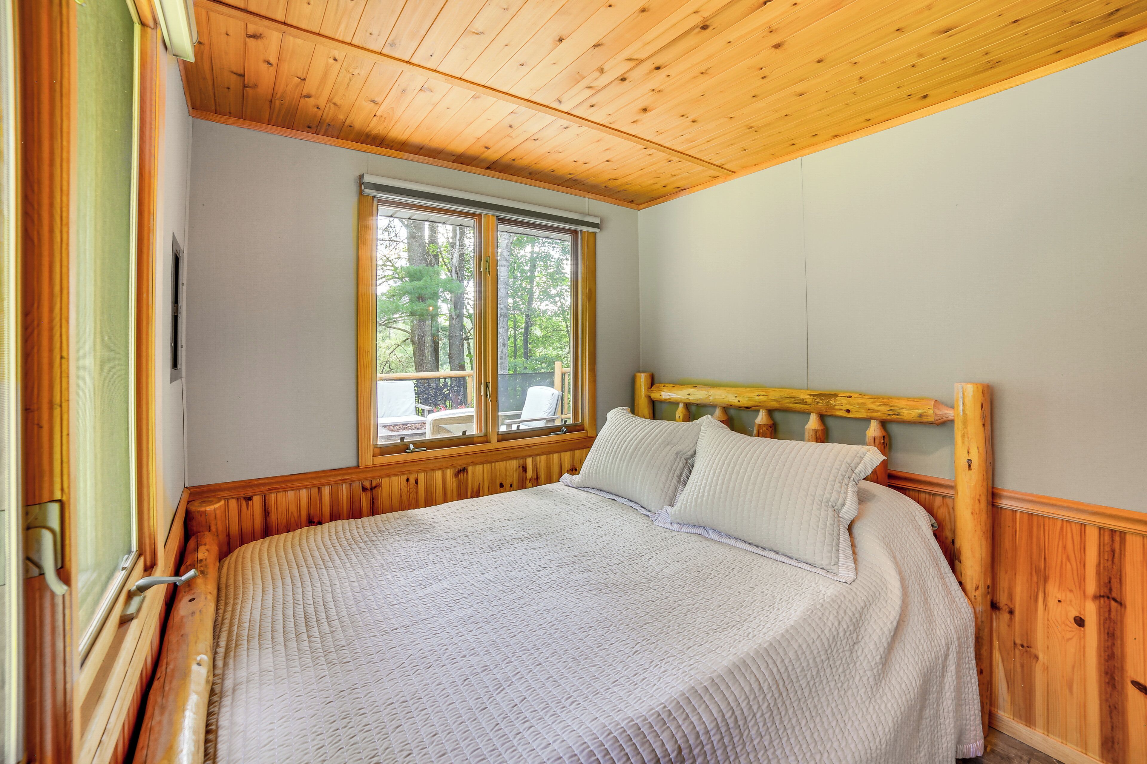 A wooden-paneled bedroom with a large bed, a window with a view of trees, and a wooden headboard.