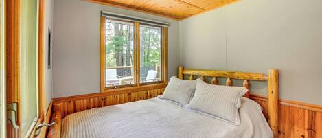 A wooden-paneled bedroom with a large bed, a window with a view of trees, and a wooden headboard.