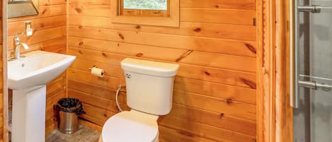 Puisesta mökistä löytyvä kylpyhuone, jossa on pesuallas, wc ja ikkuna.