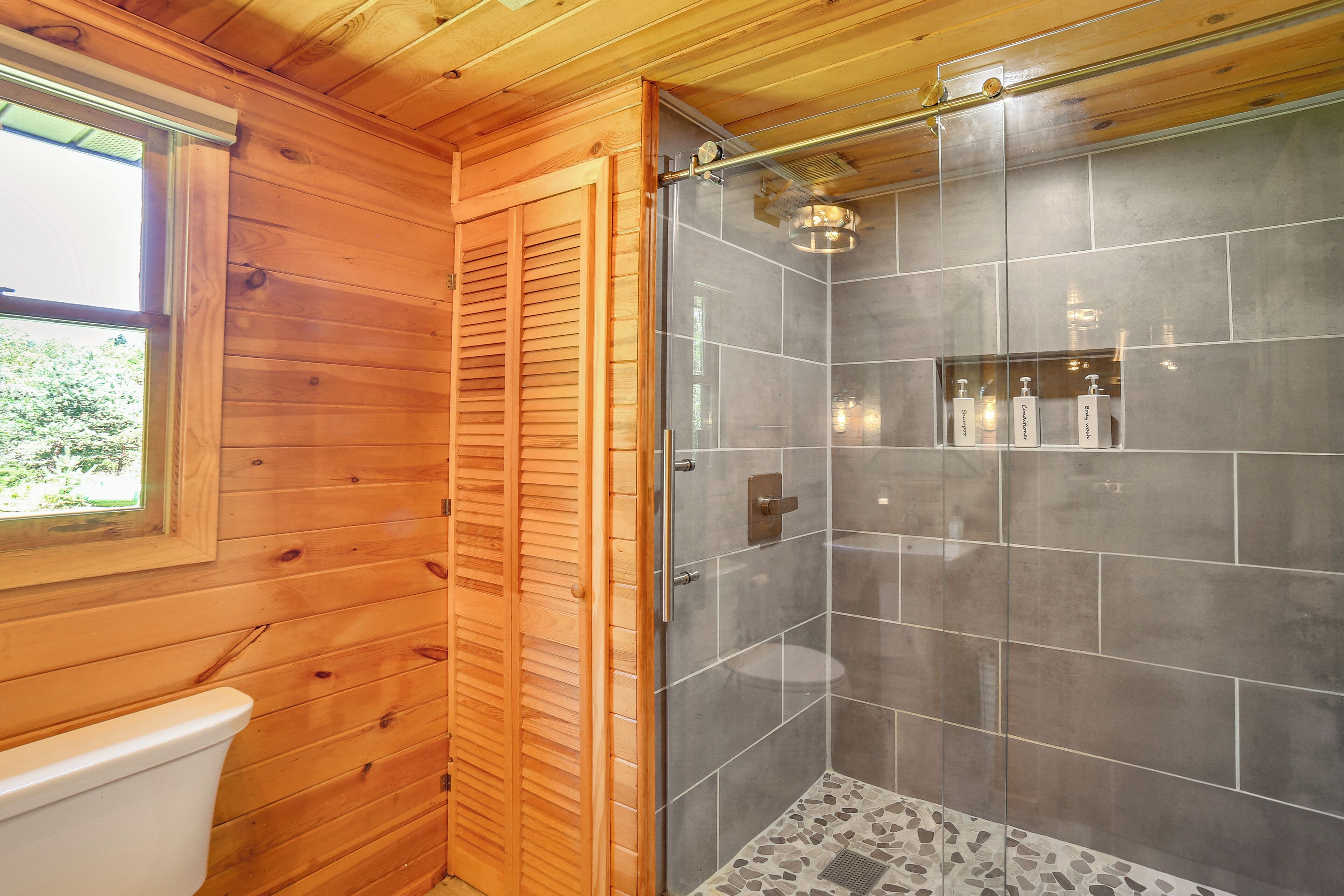 Une salle de bain aux murs lambrissés, dotée d’une douche à parois de verre et de toilettes.