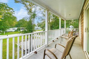 A covered porch with white railings, two wicker chairs, and a view of a green lawn and a trailer in the background. - Half Mile to Beach: Murrells Inlet Home w/ Deck! (Murrells Inlet)