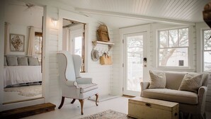 A cozy room with a white wooden interior, a white sofa, a chair, a small table, and a rug. - Water Street Cottage (Swansboro)