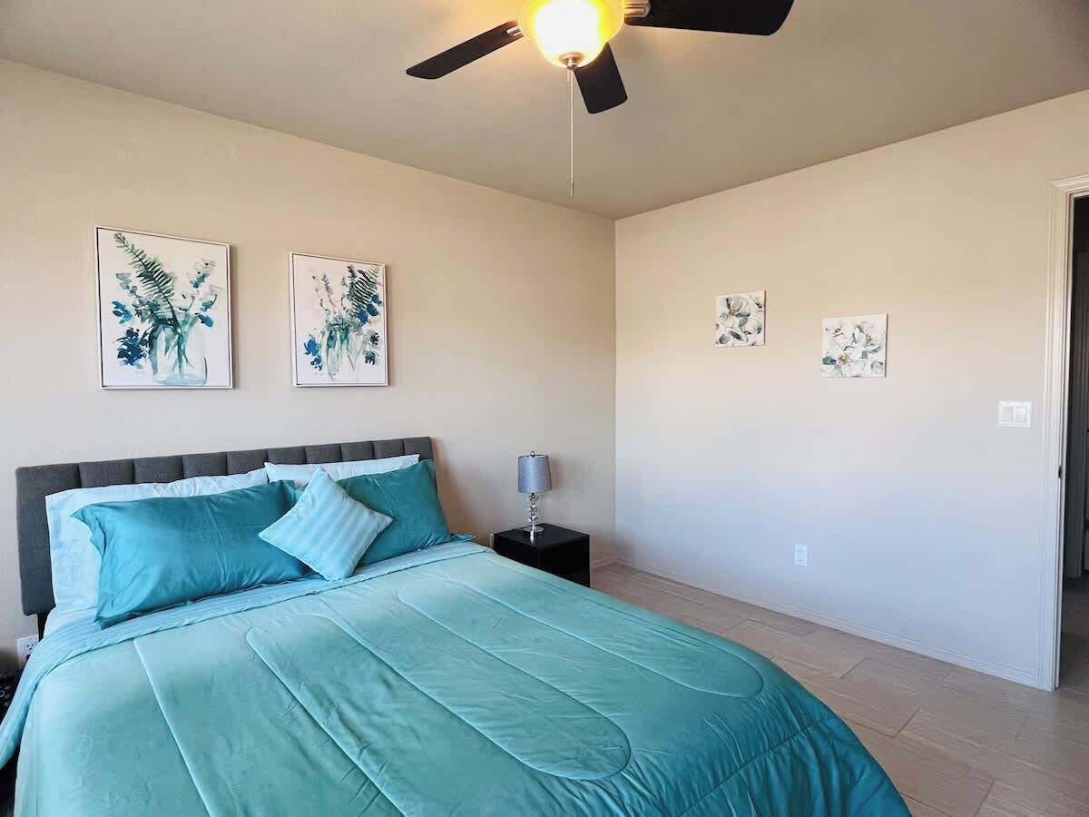 Une chambre à coucher comprenant un lit, une table de chevet, un ventilateur de plafond et des œuvres d’art murales.