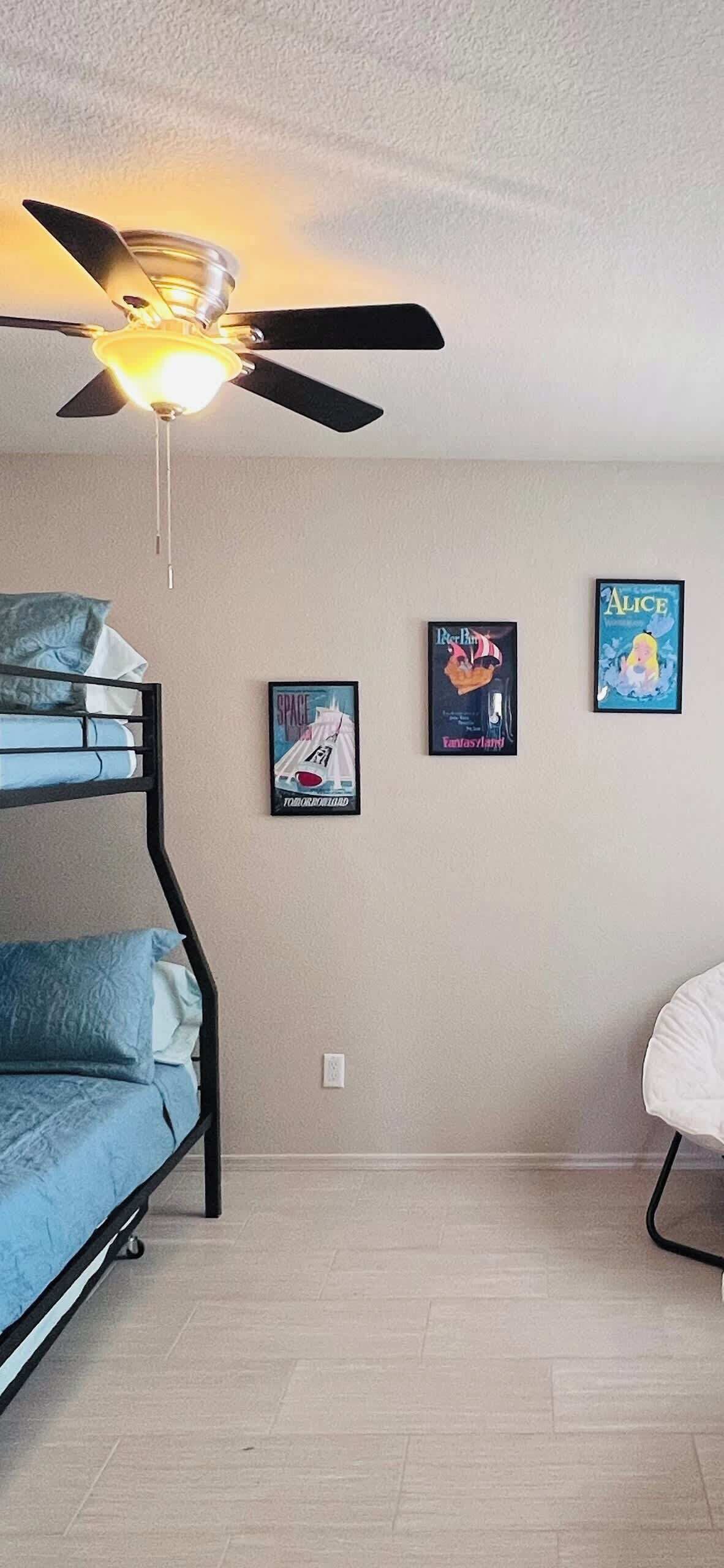 A room with bunk beds, a ceiling fan, and wall art including posters of 'Space' and 'Alice'.