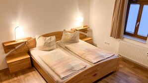 A wooden bed with two pillows, a nightstand with a lamp, and a window with curtains.