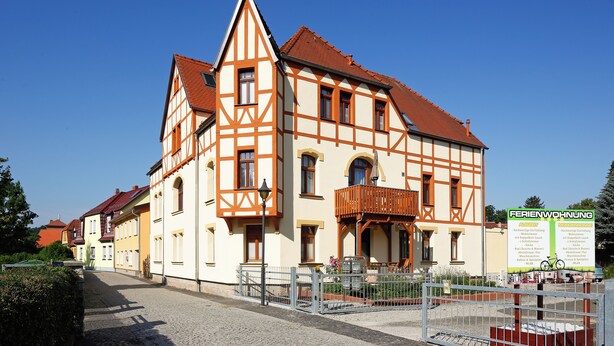 A traditional half-timbered building with a balcony, a signboard, and a cobblestone street.