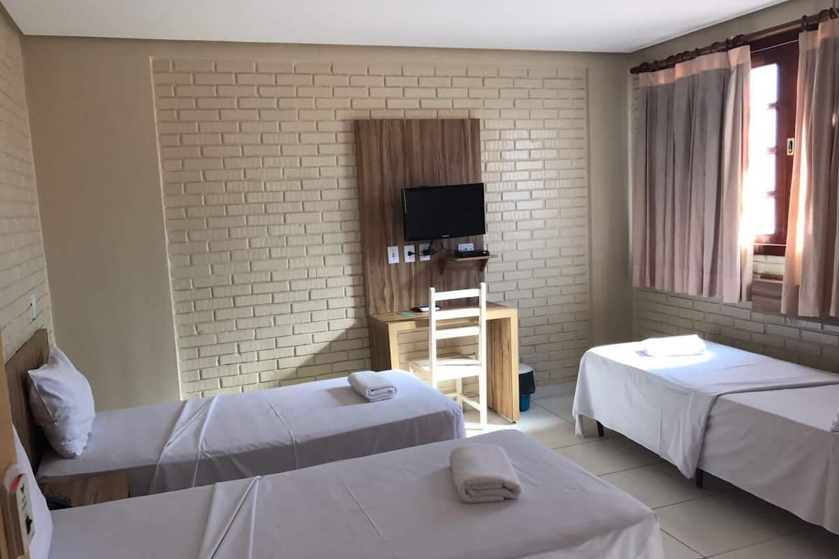Ett hotellrum med två separata sängar, en tv på ett träbord och ett fönster med gardiner.