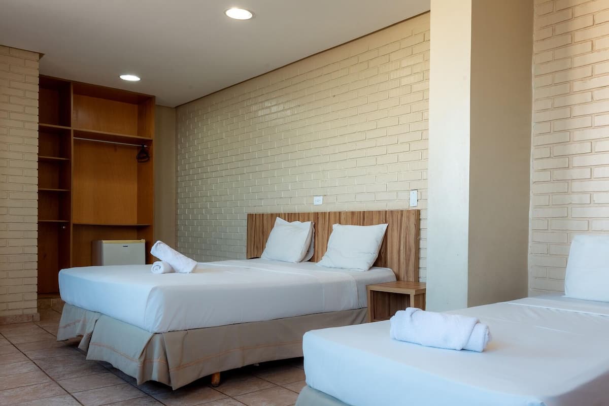Ett hotellrum med två sängar, sänggavlar i trä, en vit tegelvägg och en inbyggd garderob.
