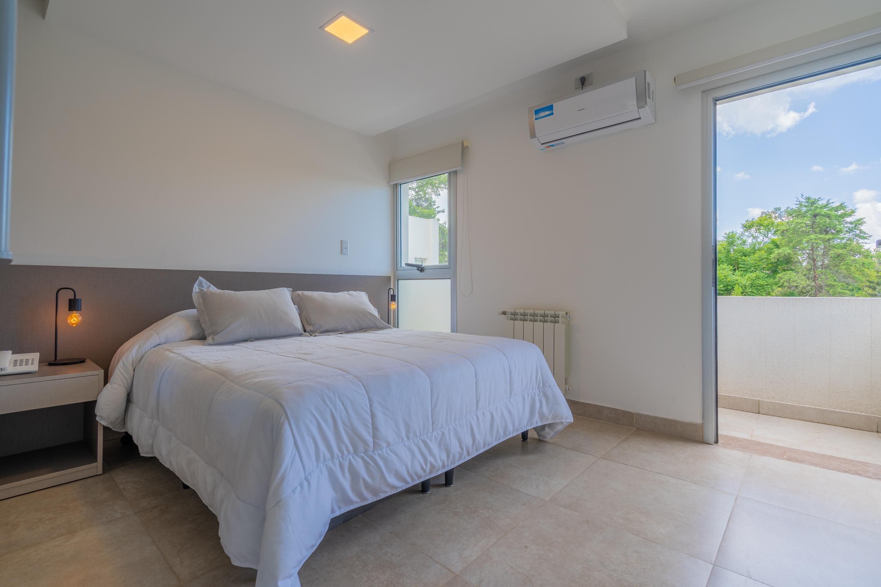 Un dormitorio moderno con una cama grande, una mesita de noche y una ventana con vistas a zonas verdes.
