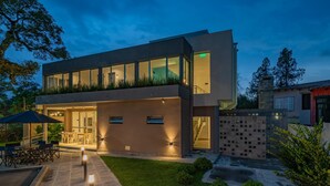 Un edificio moderno de dos plantas con tejado plano, ventanas amplias y un patio exterior bien iluminado con mesas y sillas.