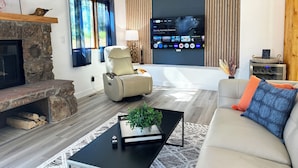 A modern living room with a stone fireplace, a comfortable sofa, a recliner, and a flat-screen TV mounted on the wall.