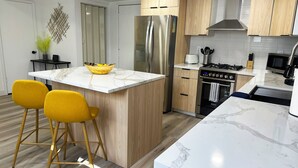 A modern kitchen with a central island, wooden cabinets, stainless steel appliances, and yellow bar stools.