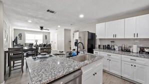 A modern kitchen with white cabinets, a granite countertop, and a dishwasher. - Modern Home Near Entertainment District, Hot Spots (Grand Prairie)