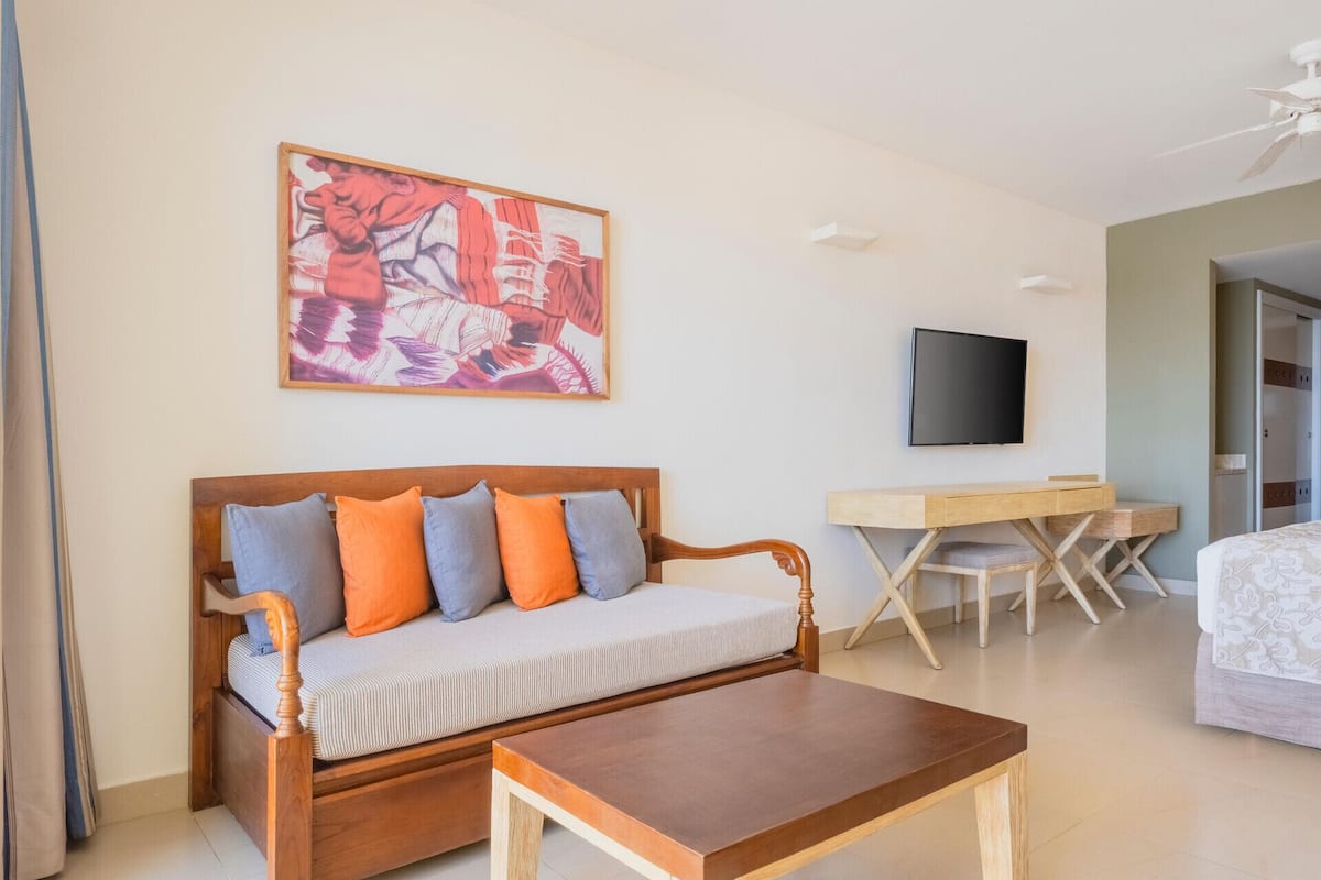 A room with a wooden sofa, a small wooden table, a TV, and a bed.