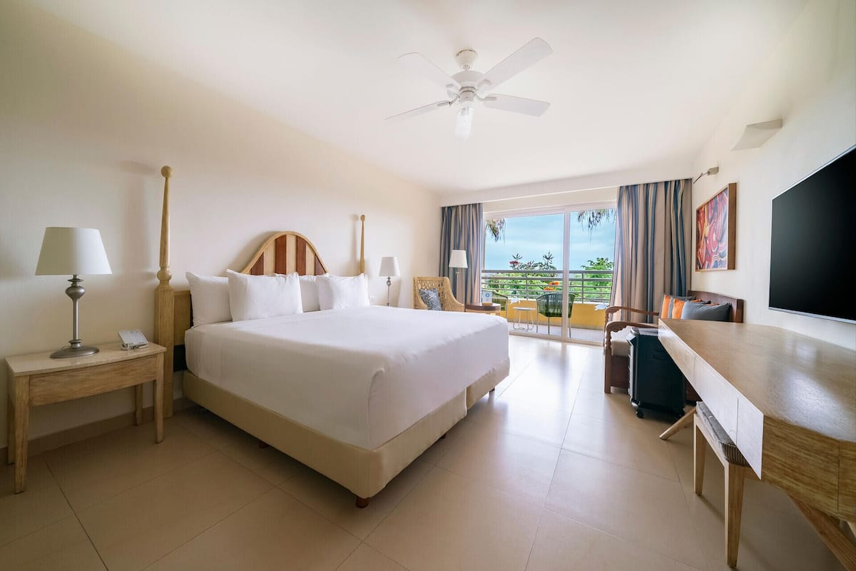 A hotel room with a bed, desk, chair, lamp, and a ceiling fan.