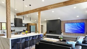A modern kitchen with a central island, bar stools, a black sofa, and a large flat-screen TV mounted on the wall. - Charming 3-bedroom house Parker (Parker)