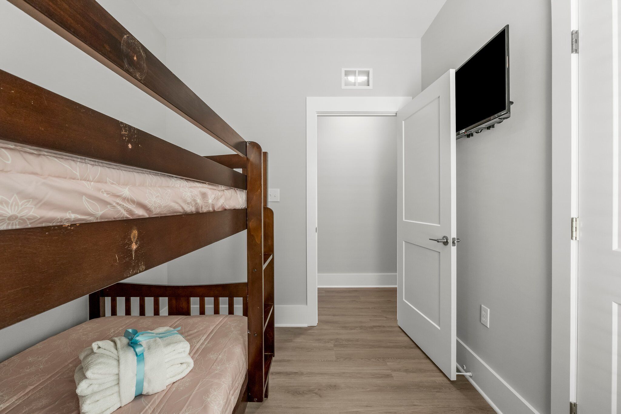 A bedroom with a bunk bed, a bedside table with a rolled towel, and a door leading to a hallway.