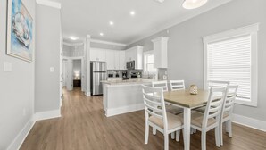 Une cuisine moderne avec des meubles blancs, des appareils en acier inoxydable et une table à manger en bois, accompagnée de chaises.