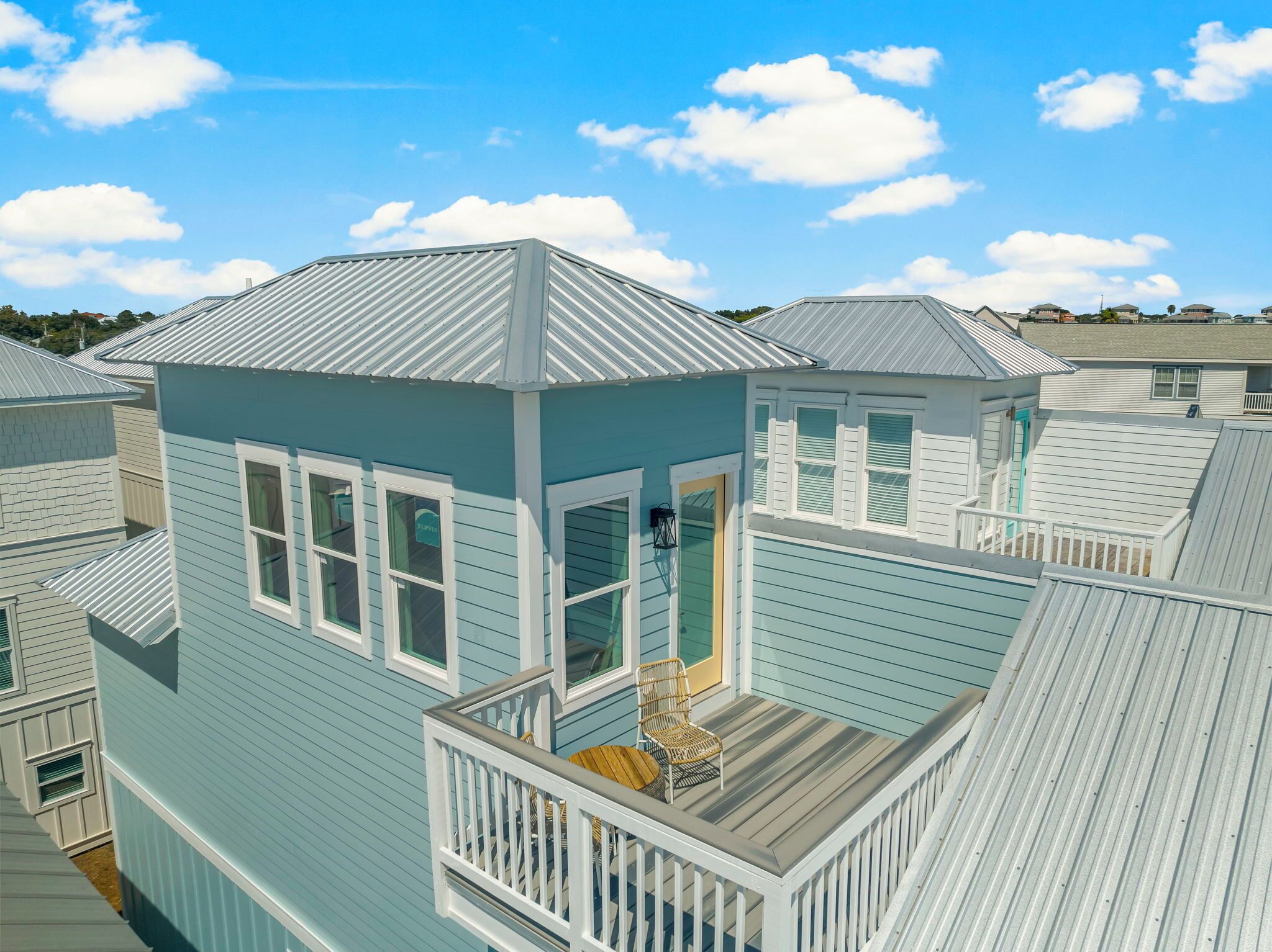 A coastal-style building with a balcony, multiple windows, and a metal roof.