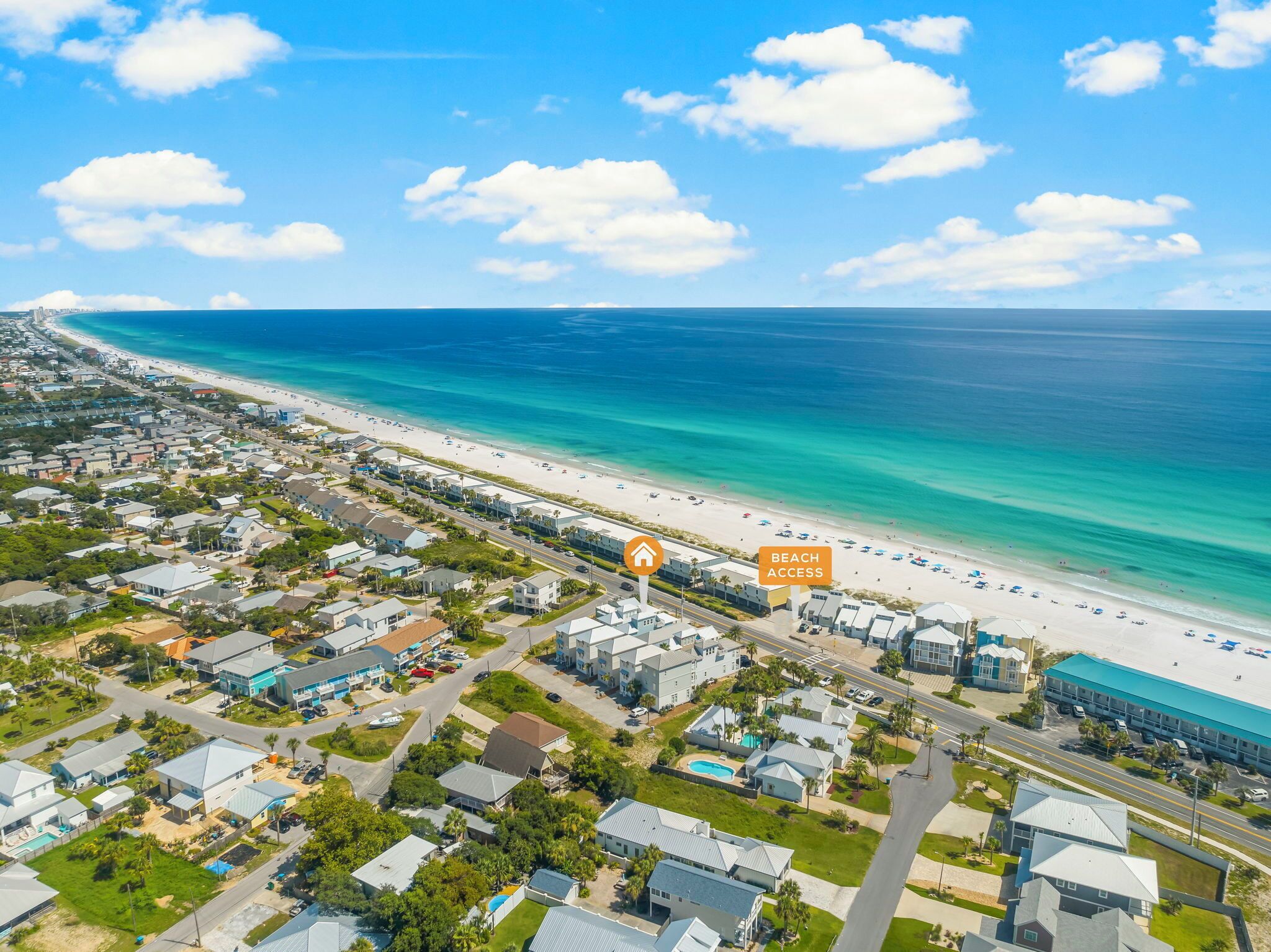 An aerial view of a coastal residential area with a beachfront, houses, and a hotel with beach access.