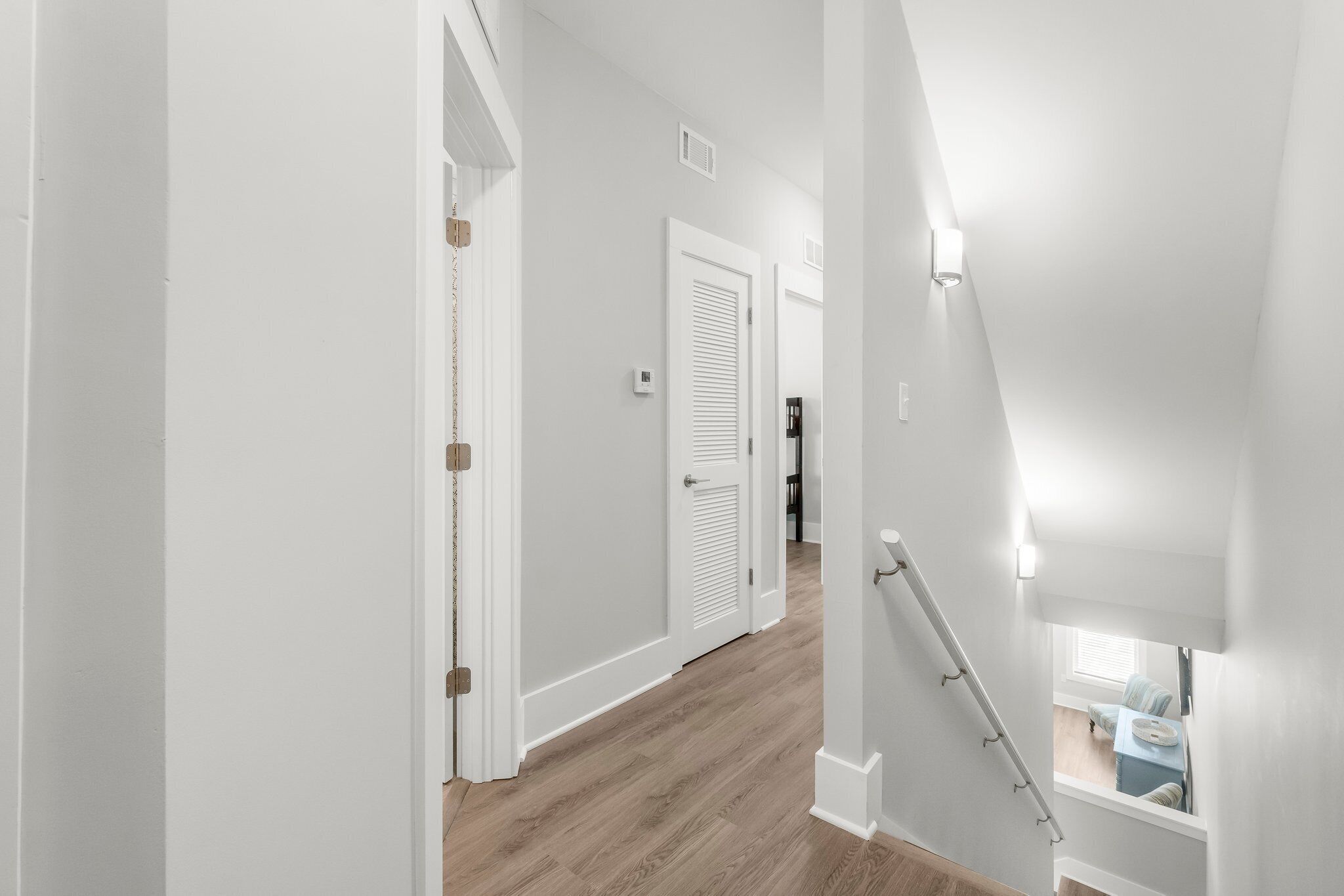 A hallway with white walls, a wooden floor, and a staircase with a handrail.