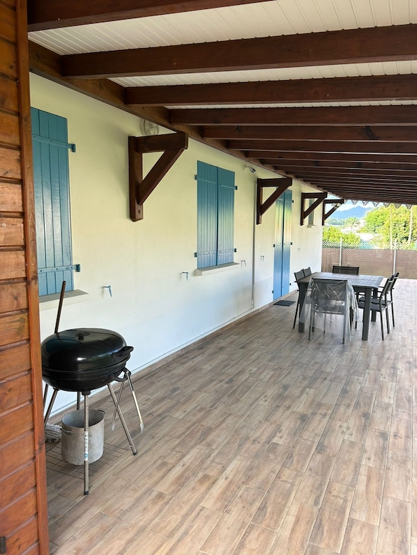 An outdoor patio with a grill, wooden flooring, and a table with chairs.