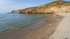 Ein Strand mit klarem Wasser, felsigen Klippen und einem unbefestigten Pfad.