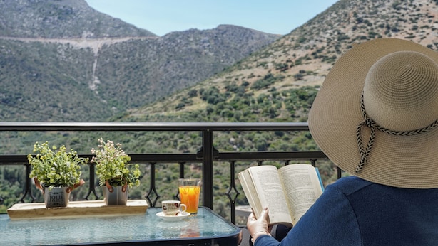 Eine Person liest ein Buch an einem Tisch mit Blick auf Berge.