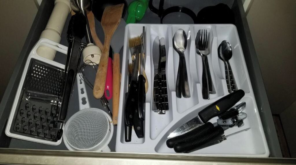 Un cajón con varios utensilios y herramientas de cocina, como un rallador, brochas, cuchillos y un juego de cucharas.