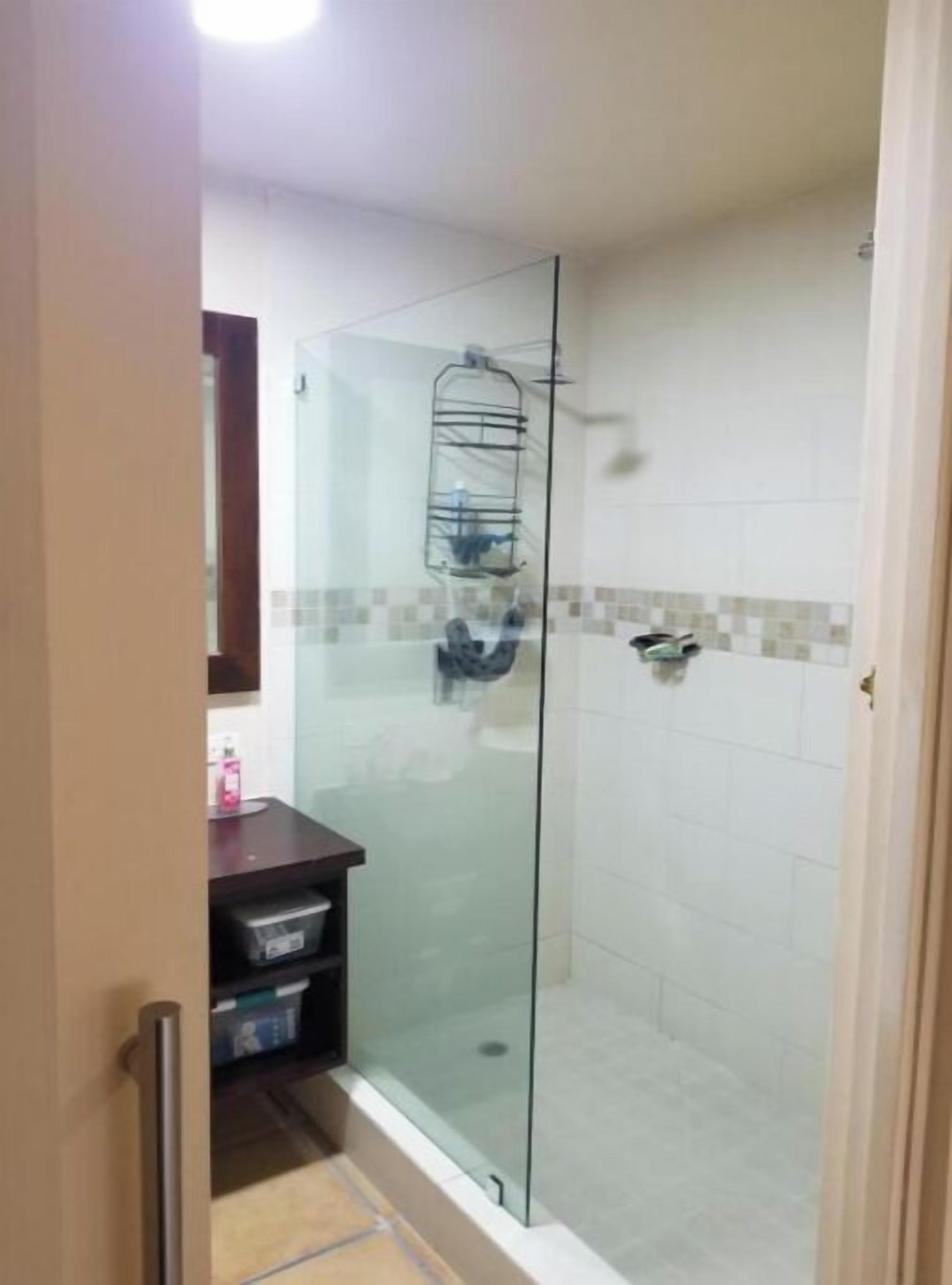 A glass-enclosed shower with a towel rack, a small shelf with toiletries, and a tiled wall.