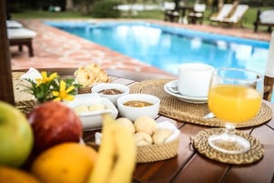 Desayuno con vistas a la piscina, que incluye frutas, pan y un vaso de zumo de naranja.