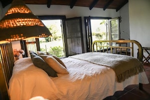 Un dormitorio con cama, lámpara colgante, ventana y vistas al verdor exterior.