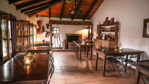 Un comedor rústico con mesas y sillas de madera, chimenea y estantes con diversos objetos.