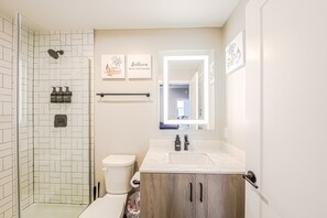 Une salle de bain moderne avec une douche à parois de verre, des toilettes blanches, un meuble-lavabo et des armoires en bois.