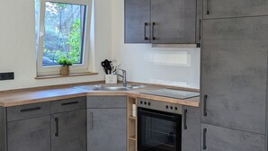 Ett modernt kök med gråa skåp, en inbyggd ugn och ett fönster med utsikt över grönområden.