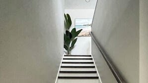 Eine moderne, minimalistisch gestaltete Treppe führt zu einem Raum mit großem Fenster mit Blick auf einen Strand.