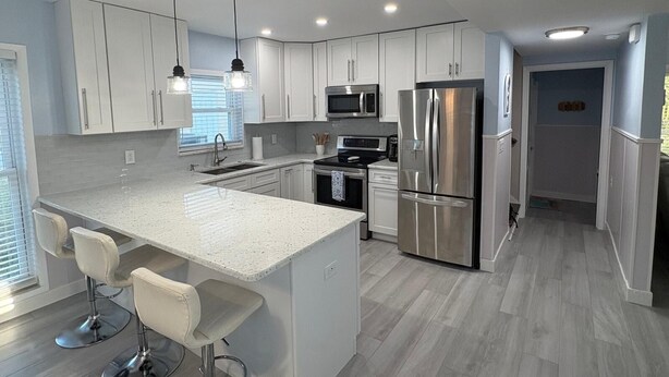 Eine moderne Küche mit weißen Schränken, Edelstahlgeräten, einer großen Kochinsel mit Barhocker und Pendelleuchten.