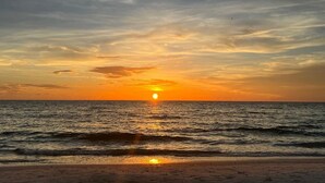 Ein Sonnenuntergang über dem Meer mit einem Strand im Vordergrund.