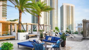A rooftop lounge with seating areas, including sofas and chairs, surrounded by potted plants and palm trees. - Stunning 25th-Floor Views in Hollywood (Hollywood)