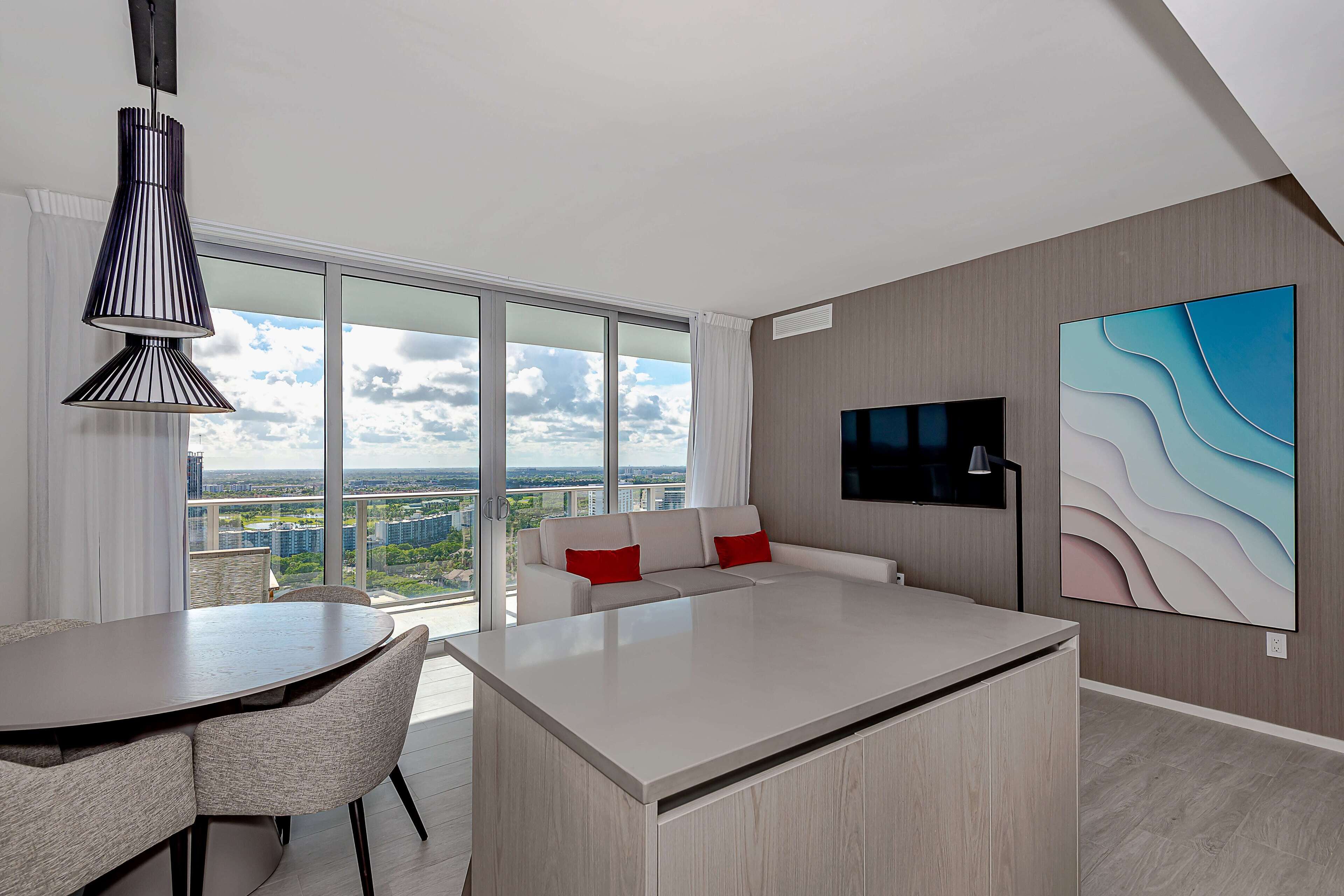 A modern living room with a large window, a sofa, a dining table, and a TV.