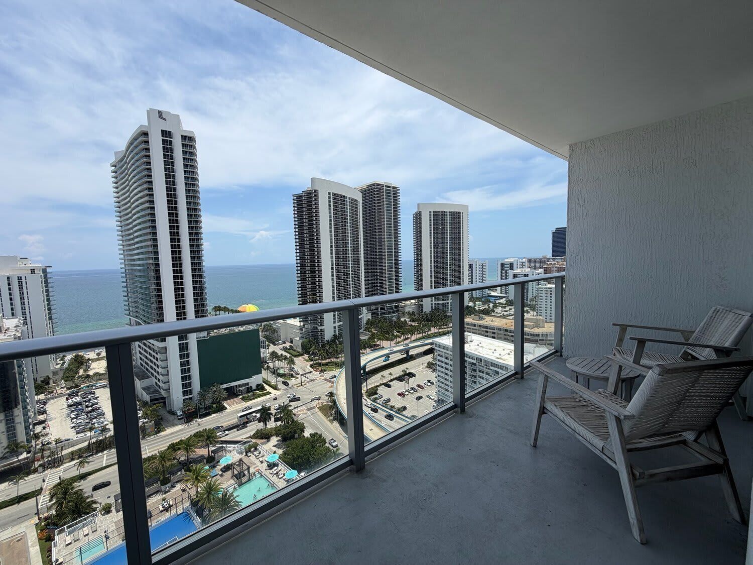 A balcony with a view of tall buildings, a swimming pool, and a clear sky.